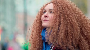 Güzel genç bir kadın kameraya bakıyor ve neşeyle gülümsüyor. Gün ışığında sokakta gülen surat. Dışarda olumlu bir portre.