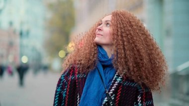 Güzel genç bir kadın kameraya bakıyor ve neşeyle gülümsüyor. Gün ışığında sokakta gülen surat. Dışarda olumlu bir portre.