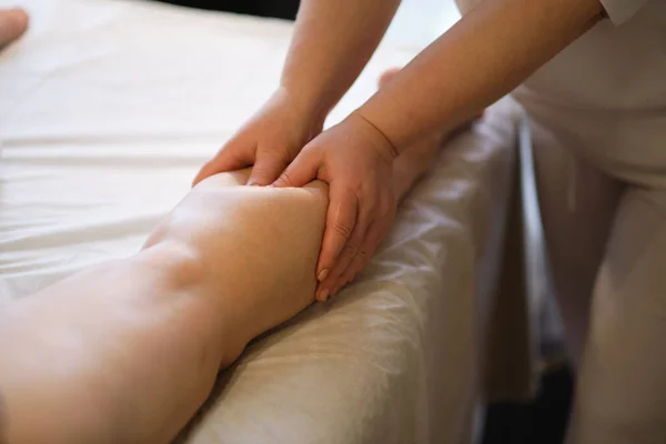 Detalle de las manos masajeando el músculo de la pantorrilla humana.Terapeuta aplicando presión sobre la pierna femenina. Manos de masajista terapeuta masajeando piernas de mujer joven en el salón de spa. Cuidado corporal en el salón de spa para mujer joven. — Foto de Stock