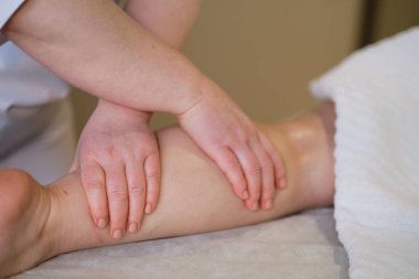 İnsan baldır kaslarına masaj yapan eller. Kadın bacağına baskı yapan terapist. Masaj terapistinin elleri masaj salonundaki genç bayanın bacaklarına masaj yapıyor. Genç bir kadın için kaplıca salonunda vücut bakımı.