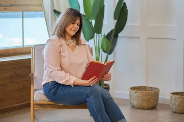 Düşünceli bayan evde bir kitap okuyor. çekici orta yaşlı kadın evde dinleniyor. Başarılı orta yaşlı kadın gülümsüyor. — Stok fotoğraf