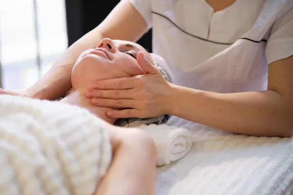 Bella ragazza ha un massaggio facciale in una clinica di bellezza. cura della pelle, concetto di spa, trattamento. Massaggio viso. Pelle facciale. Mani del massaggiatore. Donna al salone di bellezza spa. — Foto Stock