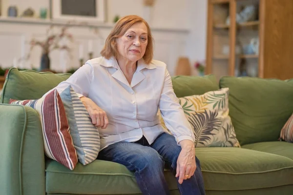 Portrait d'une femme âgée assise sur un canapé à la maison de retraite. Femme blanche assise sur un canapé et regardant la caméra. Soins aux retraités solitaires. — Photo