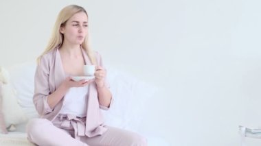 Romantik bir ortamda bir fincan kahveyle güzel genç bir kadın. Kahve fincanı olan, kanepeye oturmuş kameraya bakan kadın. seçici odak.