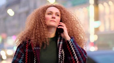 Büyük bir şehrin sokaklarında yürüyen ve telefonla konuşan bir kadın.