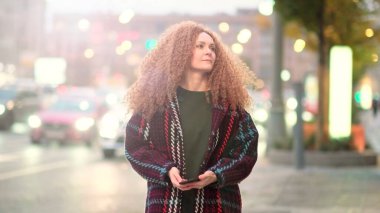 Neşeli Bayan Şehir Caddesinde yürürken cep telefonunu tutuyor. Kadın büyük bir şehrin arka planında, akşam şehrinin parlayan ışıkları..