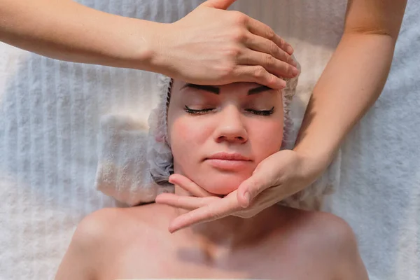 Bella ragazza ha un massaggio facciale in una clinica di bellezza. cura della pelle, concetto di spa, trattamento. Massaggio viso. Pelle facciale. Mani del massaggiatore. Donna al salone di bellezza spa. — Foto Stock