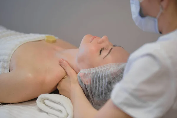 Bella ragazza ha un massaggio facciale in una clinica di bellezza. cura della pelle, concetto di spa, trattamento. Massaggio viso. Pelle facciale. Mani del massaggiatore. Donna al salone di bellezza spa. — Foto Stock