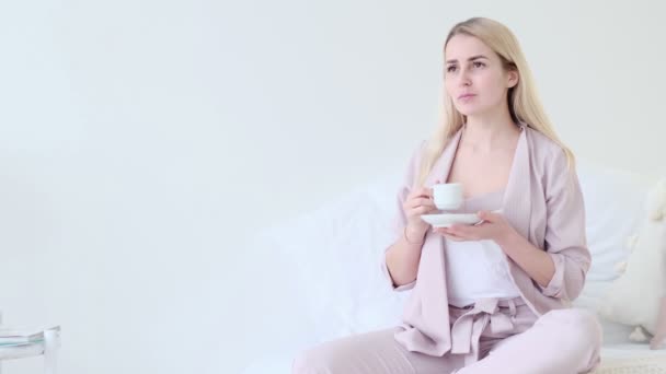 Belle jeune femme avec une tasse de café dans un cadre romantique. Femme vue de face avec tasse de café regardant la caméra assise sur un canapé. focus sélectif. — Video