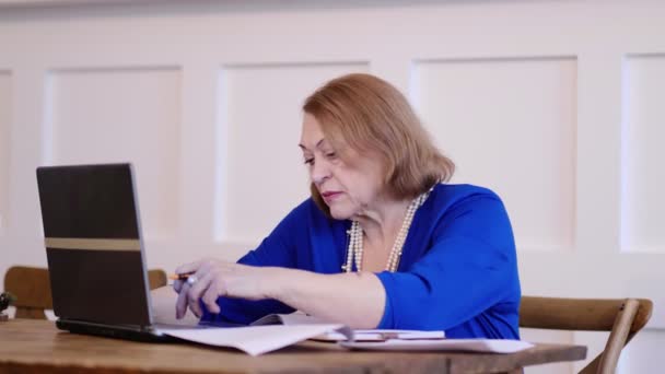 Vieille femme travaillant avec un ordinateur portable et des papiers, femme mûre occupée à payer des factures bancaires en ligne gérer les finances vérifier le budget faire de la paperasserie en utilisant l'ordinateur assis au bureau — Video