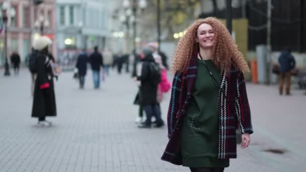 Bela jovem mulher olhando para a câmera e sorrindo alegremente. Cara feliz na rua à luz do sol. Retrato positivo lá fora. Fecha. Movimento lento — Vídeo de Stock