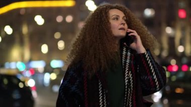 Metropolis caddesinde gece lambasıyla yürüyen ve telefonda konuşan şık ceketli güzel bir kadın..