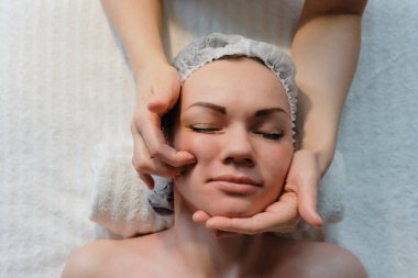 Güzel bir kızın güzellik kliniğinde yüz masajı var. Cilt bakımı, spa konsepti, tedavi. Yüz masajı. Yüz derisi. Masörün elleri. Güzellik salonundaki kadın..