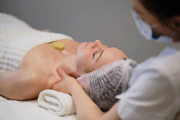 Bella ragazza ha un massaggio facciale in una clinica di bellezza. cura della pelle, concetto di spa, trattamento. Massaggio viso. Pelle facciale. Mani del massaggiatore. Donna al salone di bellezza spa. — Foto Stock