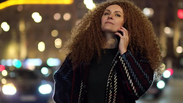 Metropolis caddesinde gece lambasıyla yürüyen ve telefonda konuşan şık ceketli güzel bir kadın..