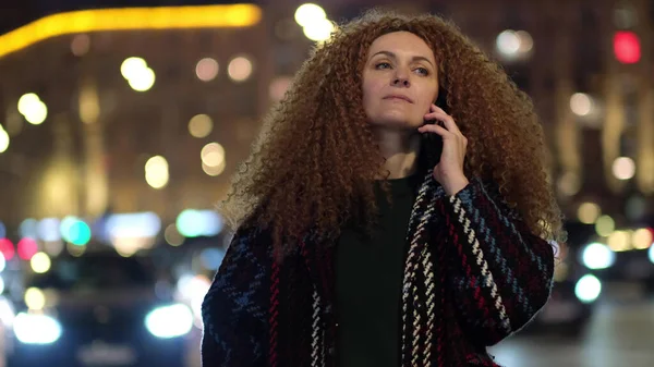 Bonita mulher na moda casaco andando na rua metrópole com luzes da noite e falando ao telefone. — Fotografia de Stock