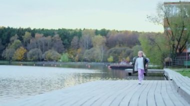 Sarışın kız öne doğru koşar. Küçük kız ormanın yakınında eğleniyor. Çocuk güneşli bir günde sonbahar ormanının dışında koşuyor ve dönüyor..