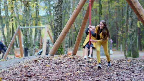 Petite fille qui s'amuse dehors. Zipline pour les enfants. Des images au ralenti. maman ou nounou joue avec sa fille sur le terrain de jeu. concept d'enfance heureuse. — Video