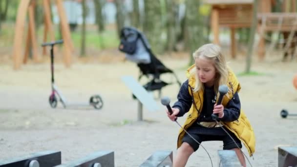 Maman ou nounou joue avec sa fille sur le terrain de jeu. concept d'enfance heureuse. petite fille jouant des instruments de musique de rue — Video