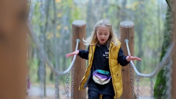 Drôle de petite fille courant vers la caméra sur un pont de corde dans le parc. défocalisation. — Video
