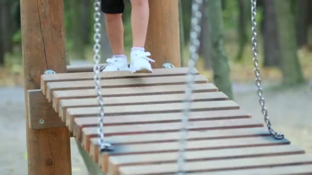 Großaufnahme von Kinderfüßen auf der schwingenden Holzbrücke am Spielplatz im Park. Kinder spielen auf einem Kinderspielplatz. Defokus — Stockvideo
