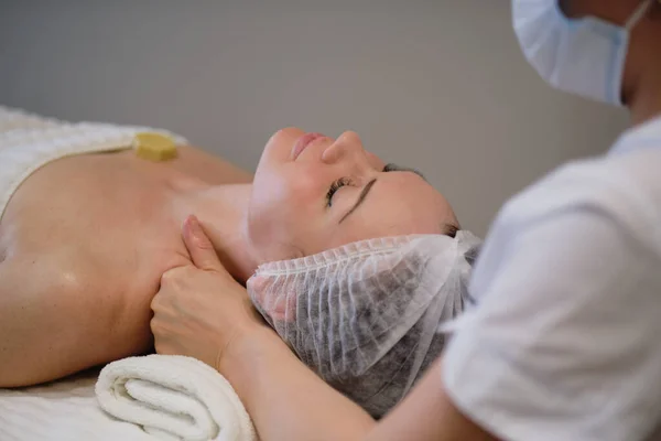 Bella ragazza ha un massaggio facciale in una clinica di bellezza. cura della pelle, concetto di spa, trattamento. Massaggio viso. Pelle facciale. Mani del massaggiatore. Donna al salone di bellezza spa. — Foto Stock