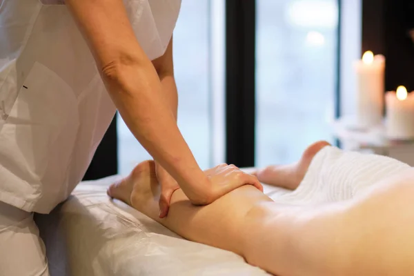 Detail of hands massaging human calf muscle.Therapist applying pressure on female leg. Hands of massage therapist massaging legs of young woman in spa salon. Body care in spa salon for young woman. — Stock Photo, Image