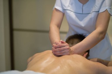 İnsanın rahatlatıcı omuz masajından zevk aldığı yakın çekim. Masaj masasında dinlenen adam masaj yaptırıyor.