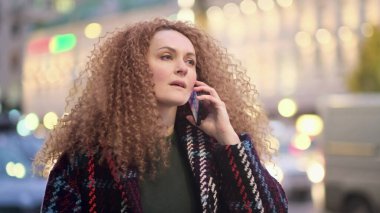 Büyük bir şehrin sokaklarında yürüyen ve telefonla konuşan bir kadın.