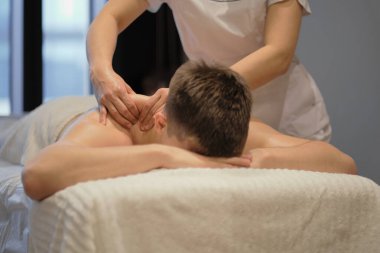 İnsanın rahatlatıcı omuz masajından zevk aldığı yakın çekim. Masaj masasında dinlenen adam masaj yaptırıyor.