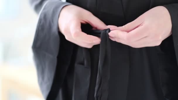 Mujer en túnica de seda negra ata cinturón en su túnica. Vista de cerca. Vídeo en cámara lenta. material de archivo — Vídeos de Stock