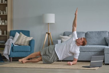 Genç aktif adam dizüstü bilgisayarda video eğitimi izliyor, egzersiz yapıyor, sabah evde egzersiz yapıyor. Spor, sağlıklı yaşam tarzı. Evde Forma gir.