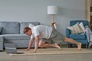 Evde kalırken kendine dikkat et. Spor eğitimi, evde dizüstü bilgisayarlı erkekler için esneme egzersizleri. Fitness minderinde yatan adam çevrimiçi yoga dersleri boş laptop ekranı