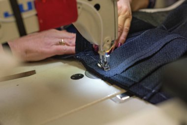 İş yerindeki profesyonel üretim makinesine beyaz kumaş diken kadın elleri. Dikiş işleminin görüntüsünü kapat. Işık bulanık arkaplan