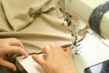İş yerindeki profesyonel üretim makinesine beyaz kumaş diken kadın elleri. Dikiş işleminin görüntüsünü kapat. Işık bulanık arkaplan