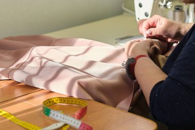 Elbise dikmek için tekstil işinde çalışan yetenekli bir kadın terzi. Dikiş işleminin görüntüsünü kapat. Işık bulanık arkaplan