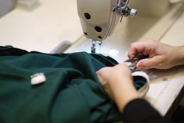 İş yerindeki profesyonel üretim makinesine beyaz kumaş diken kadın elleri. Dikiş işleminin görüntüsünü kapat. Işık bulanık arkaplan