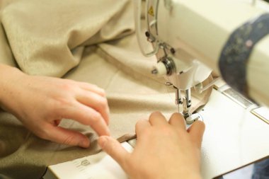 İş yerindeki profesyonel üretim makinesine beyaz kumaş diken kadın elleri. Dikiş işleminin görüntüsünü kapat. Işık bulanık arkaplan