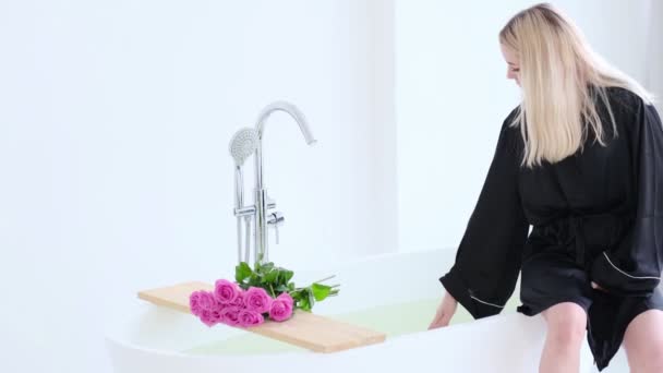 Giovane bella donna prende l'acqua nel bagno. Lussuoso bagno in marmo bianco che scorre acqua alla vasca da bagno con rosa Rosa. Weekend romantico in hotel. Video al rallentatore. Filmati stock 4k di alta qualità. — Video Stock