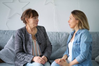 Yetişkin kızı yaşlı annesiyle konuşuyor. Anne ve kızı sohbetten zevk alıyorlar modern oturma odasındaki koltukta oturuyorlar. veli ilişkisi kavramı