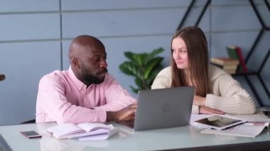 Modern bir ofiste masa başında oturmuş laptopla konuşan çeşitli iş arkadaşları.