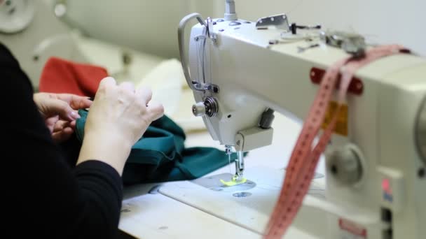 Kvinnliga händer sy tyg på professionell tillverkningsmaskin på arbetsplatsen. Närbild av syprocessen. ljus suddig bakgrund — Stockvideo