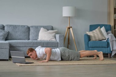 Evde kalırken kendine dikkat et. Spor eğitimi, evde dizüstü bilgisayarlı erkekler için esneme egzersizleri. Fitness minderinde yatan adam çevrimiçi yoga dersleri boş laptop ekranı