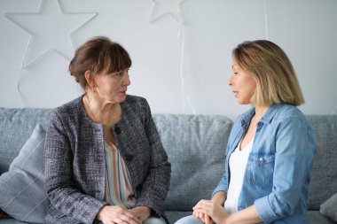 Yetişkin kızı yaşlı annesiyle konuşuyor. Anne ve kızı sohbetten zevk alıyorlar modern oturma odasındaki koltukta oturuyorlar. veli ilişkisi kavramı