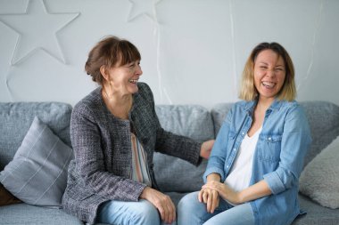 Yaşlı anne ve kız sohbetten zevk alıyor modern oturma odasındaki kanepede oturuyor. Yaşlılara hitap etmek. Yaşlı anne ve orta yaşlı kızın birlikte gülümseyen portresi.