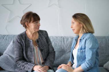 Yetişkin kızı yaşlı annesiyle konuşuyor. Anne ve kızı sohbetten zevk alıyorlar modern oturma odasındaki koltukta oturuyorlar. veli ilişkisi kavramı