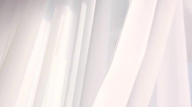 Perdelerin arasından sabah güneşiyle aydınlık bir pencere. Beyaz yatak odasındaki soyut beyaz dalgalı perde.