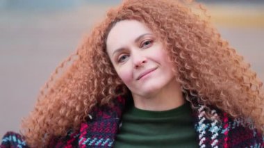 Güzel genç bir kadın kameraya bakıyor ve neşeyle gülümsüyor. Gün ışığında sokakta gülen surat. Dışarıda olumlu bir portre var. Kapatın. Yavaş çekim videosu. depolama görüntüleri