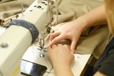 İş yerindeki profesyonel üretim makinesine beyaz kumaş diken kadın elleri. Dikiş işleminin görüntüsünü kapat. Işık bulanık arkaplan