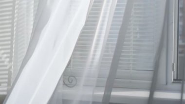 Odadaki açık pencereden rüzgar esiyor. Pencerenin yanında beyaz tül sallıyor.
